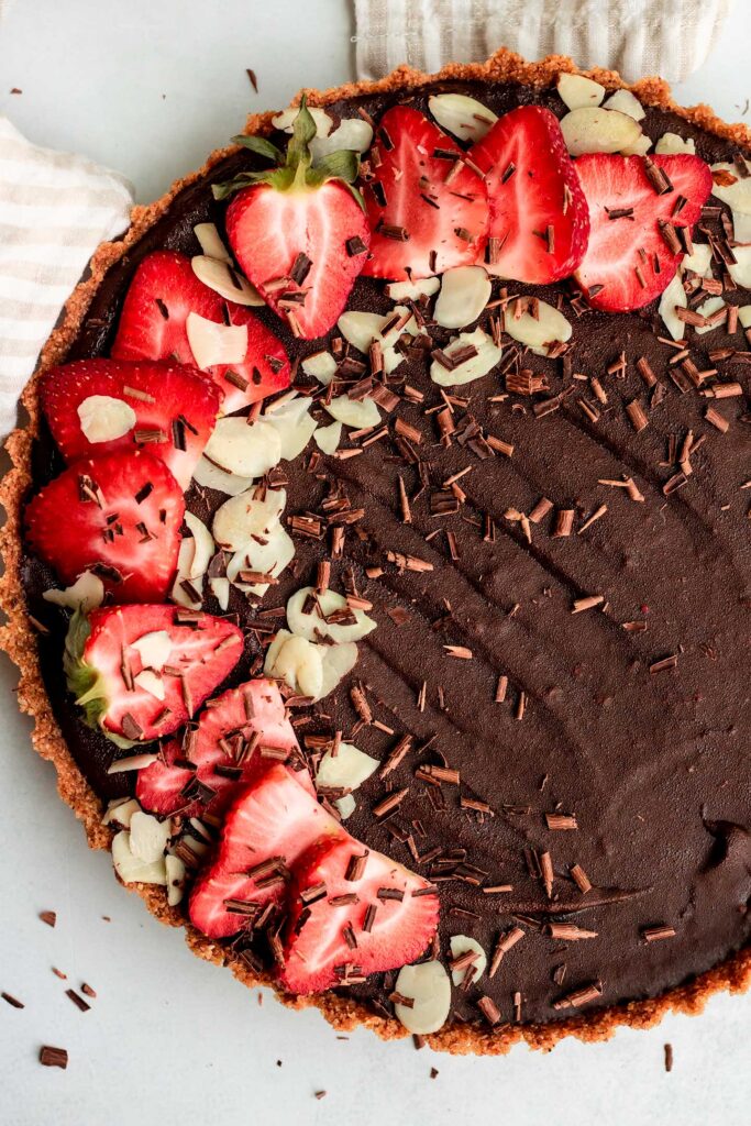 TTop down view of the chilled chocolate tart topped with almond slices and fresh sliced strawberries.