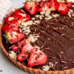 Side view of the chocolate tart topped with strawberry slices, almond slices and shaved chocolate.