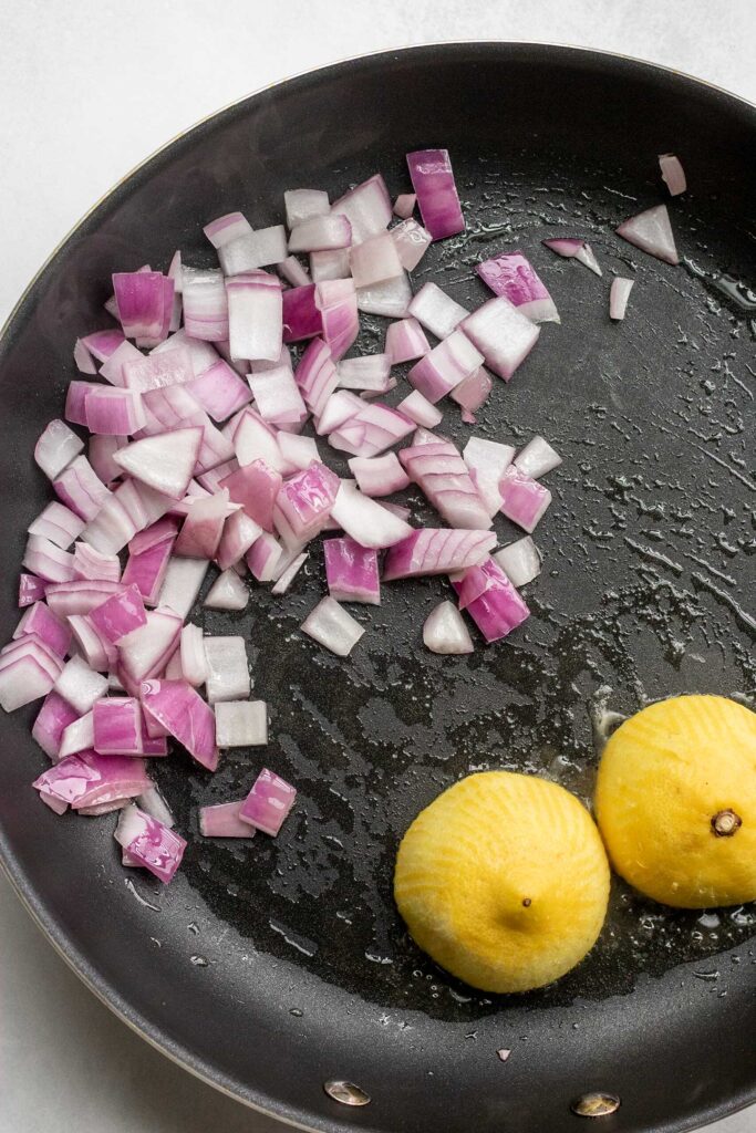Cooked onion in a pan with seared lemon halves.