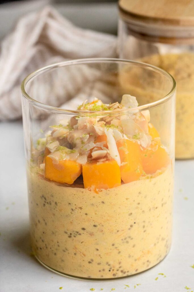 Jar of mango milk blended overnight oats topped with fresh mango, coconut flakes and zested lime.