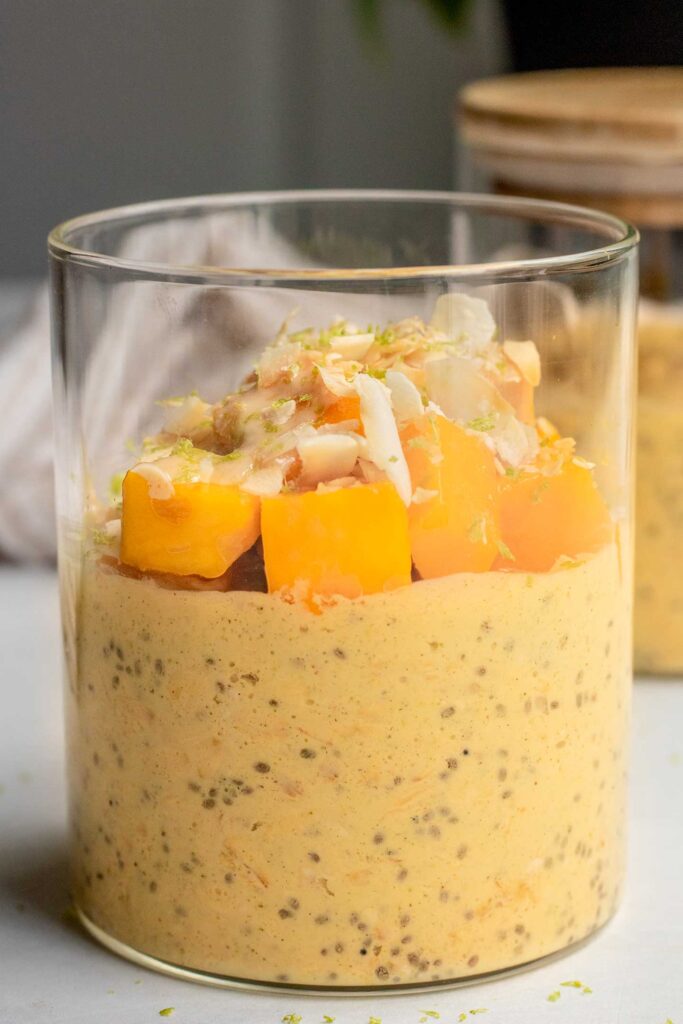 Front view of a jar filled with mango flavored overnight oats topped with fresh cubed mango and toasted coconut flakes.
