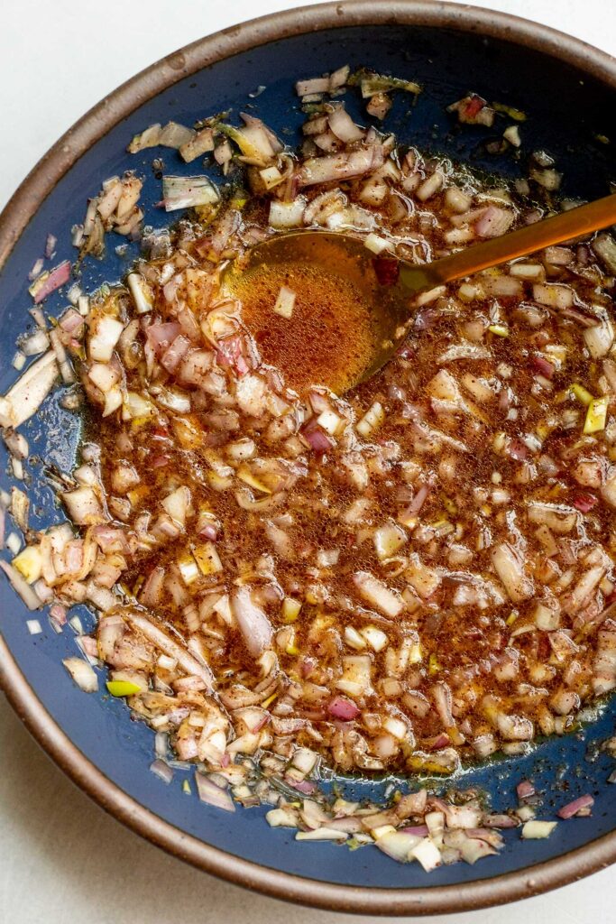 Marinade of seared lemon juice, red wine vinegar, shallots, garlic and maple syrup mixed together in a blue bowl.