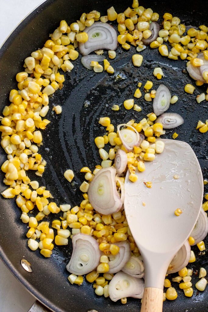 Sautéing corn and shallots together in a black pan.
