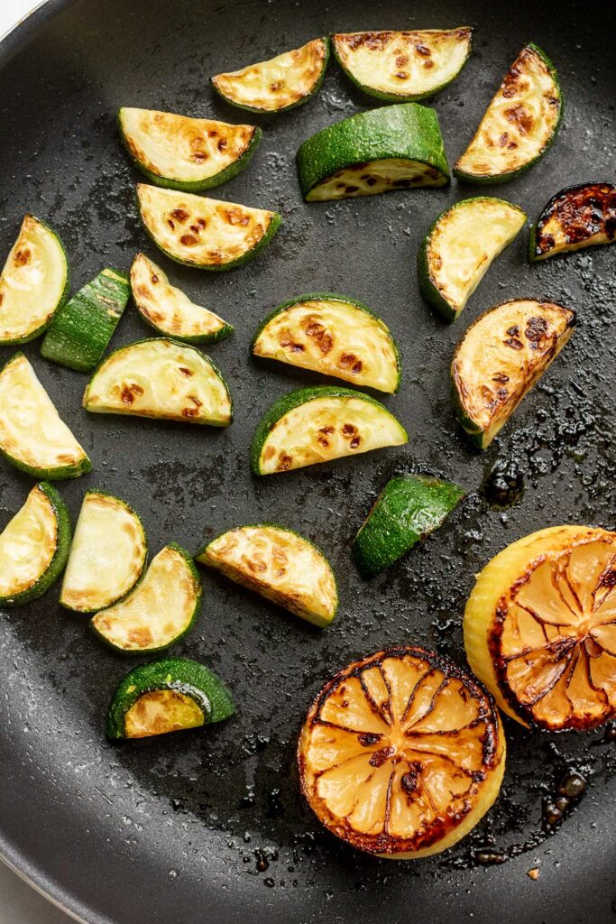 Seared zucchini halves and lemon halves in a pan.