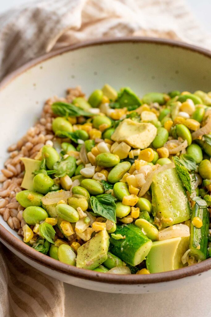 Side view of a bowl of farro topped with edamame corn salad tossed in an herby citrus vinaigrette.