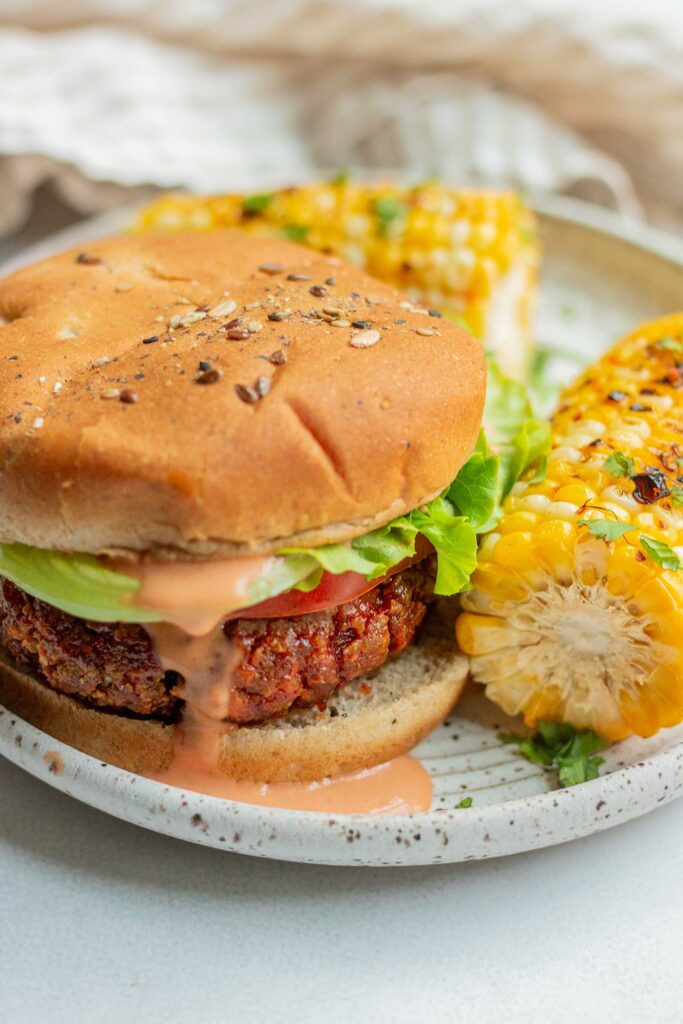 Close up of a plate loaded with grilled corn and a tofu burger.