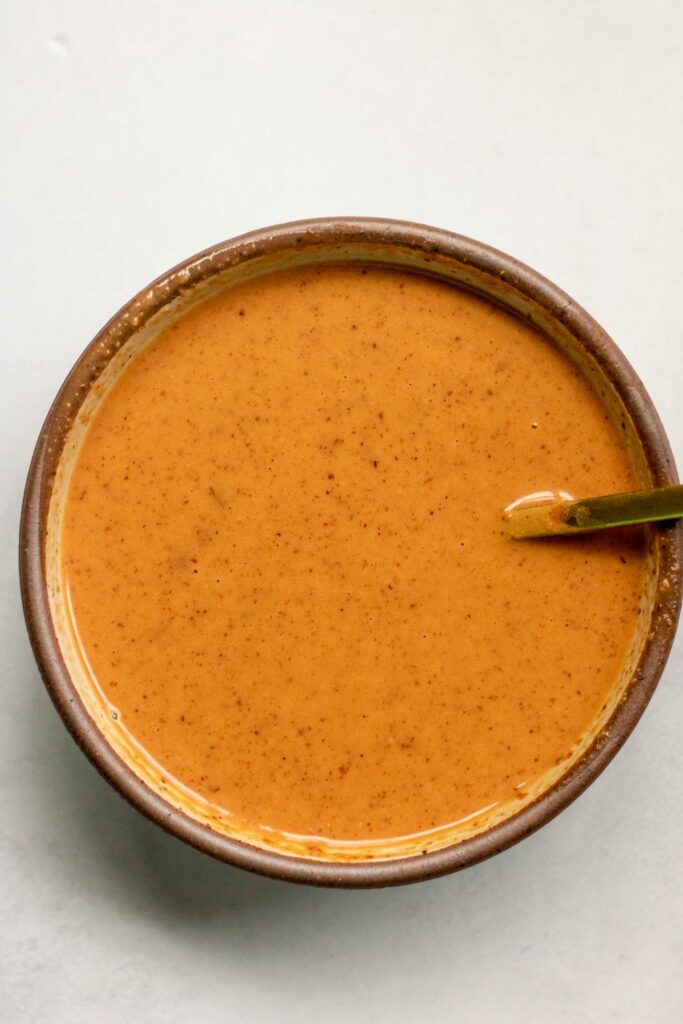 Sweet chili almond butter dressing in a bowl being mixed with a spoon.