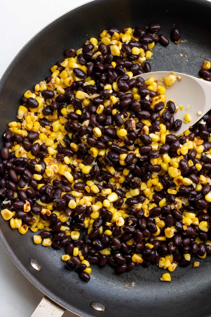 Sautéing black beans and corn in a skillet with a spatula.