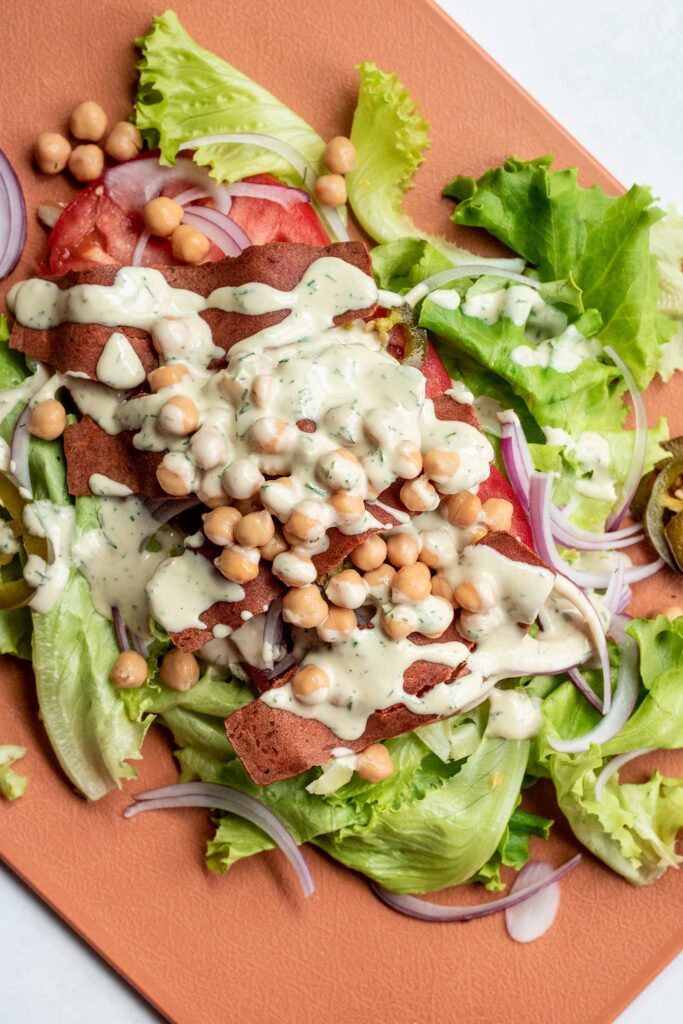 A cutting board layered with lettuce, tomatoes, onions, chickpeas, LightLife Smart Bacon strips, chickpeas and tahini ranch.