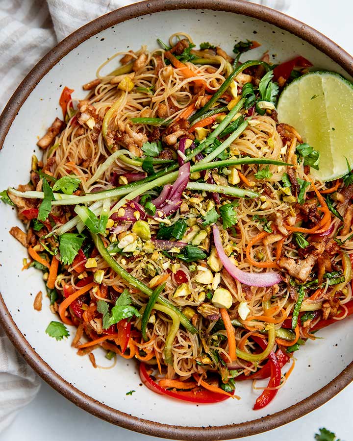 Top down shot of a cold noodle salad mixed with shredded carrots, cucumbers, tofu, bell pepper and pickled onions.