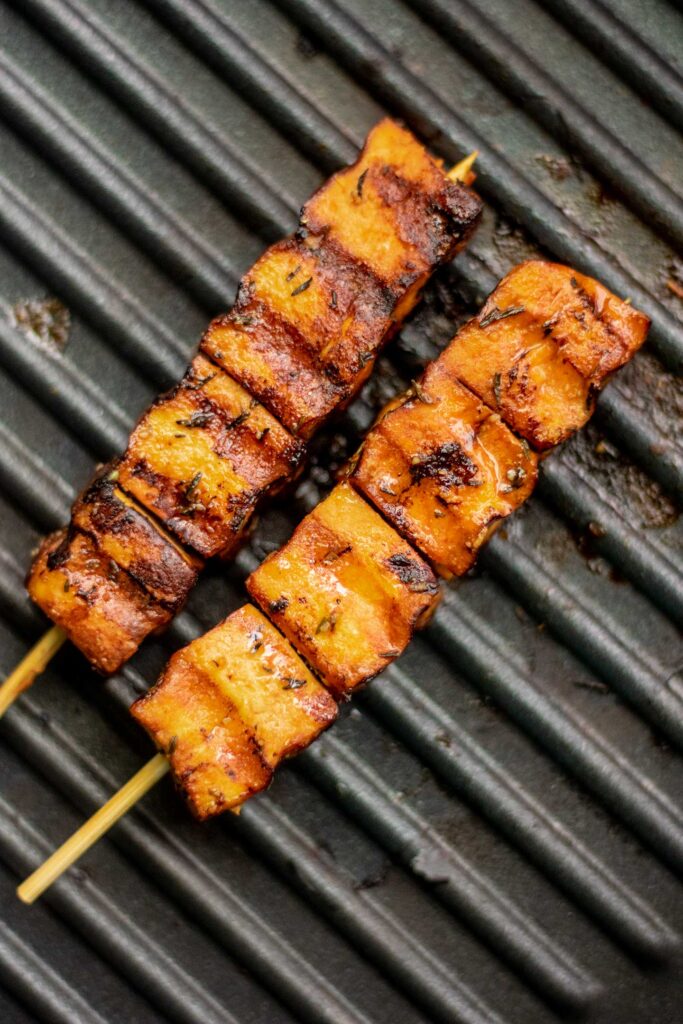 Grilled skewered tofu cooking on a grill pan.
