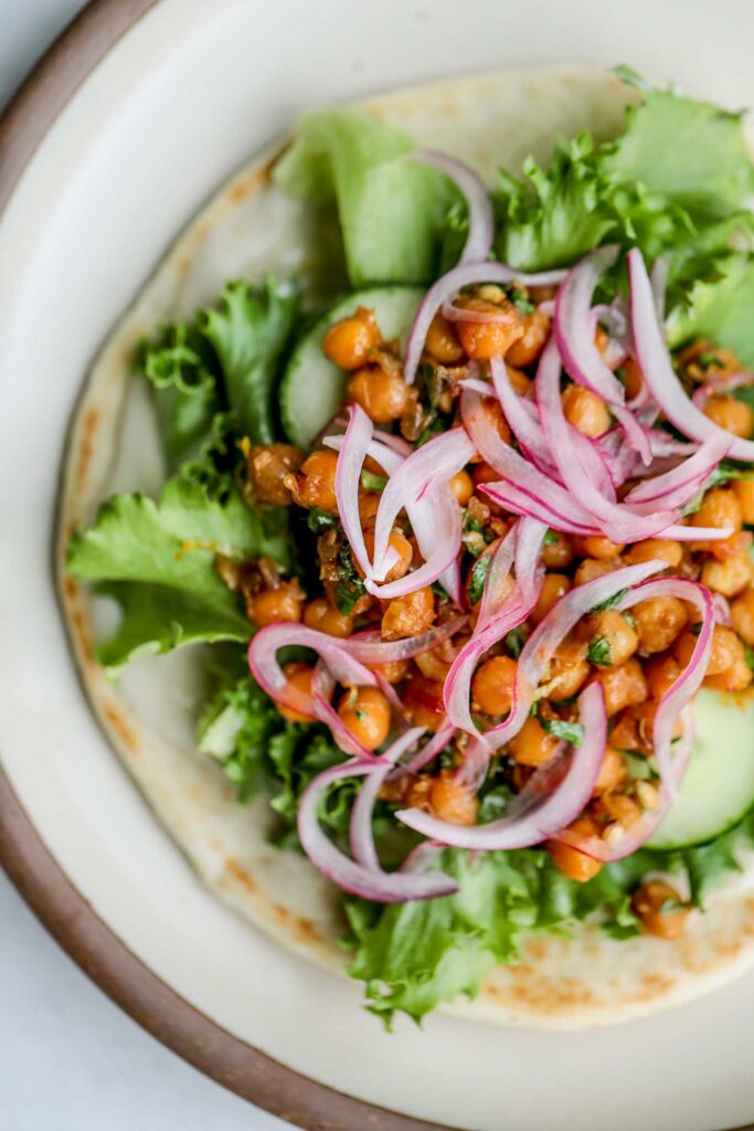 Layering a pita with lemon yogurt sauce, greens, cucumber slices, sticky chickpeas, and pickled red onions.