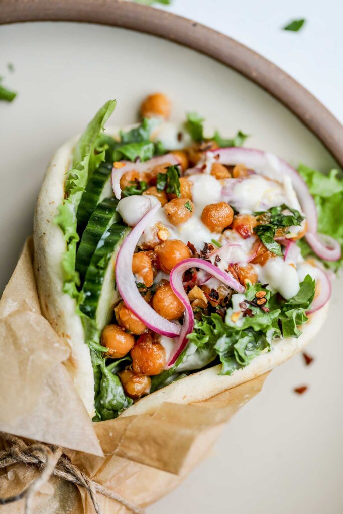 Sticky lemon chickpeas stuffed into a pita wrap loaded with greens, cucumber slices, yogurt sauce and pickled onions.