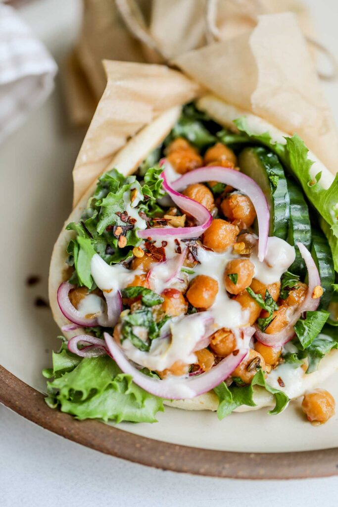 A chickpea pita wrap stuffed with lettuce, cucumber slices, pickled onions and a lemon yogurt sauce.