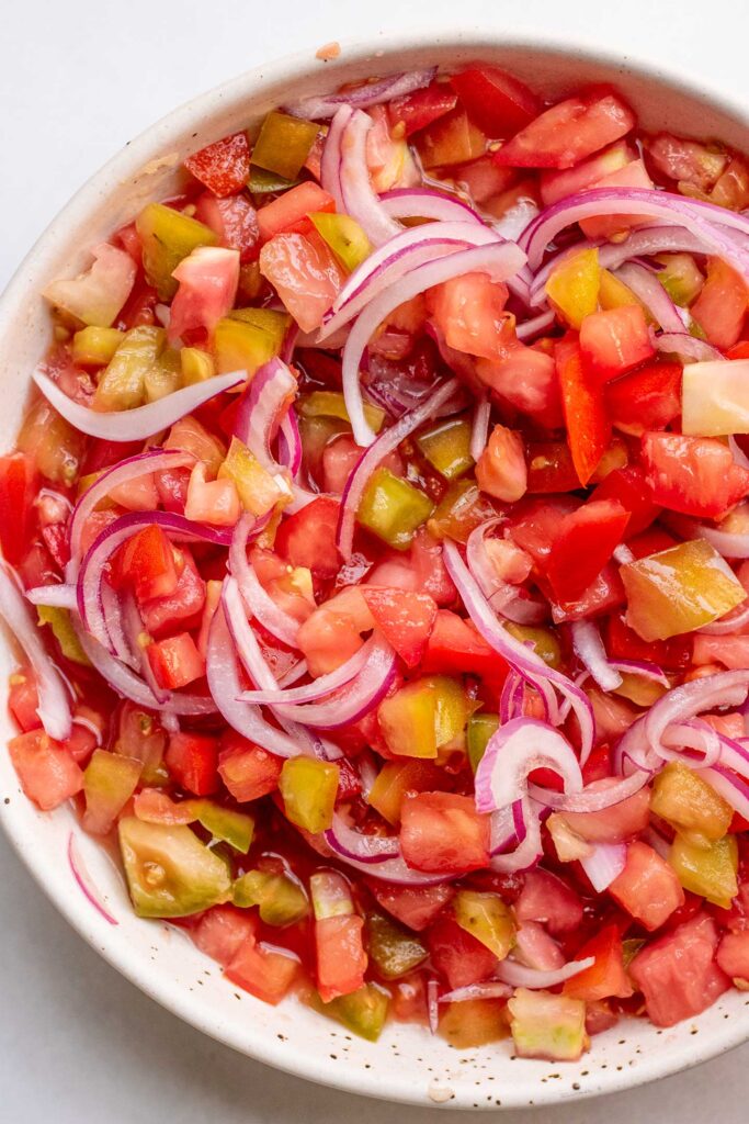 Bowl of fully mixed tomato salad with red onions.