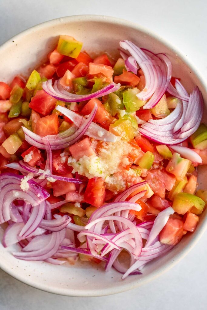 Bowl filled with diced tomatoes, sliced red onions, garlic and dressing.