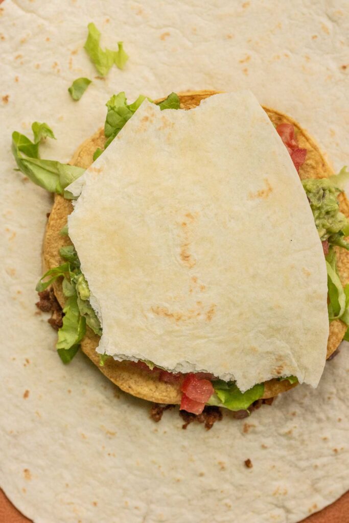Placing a broken tortilla on top of the wrap filling.