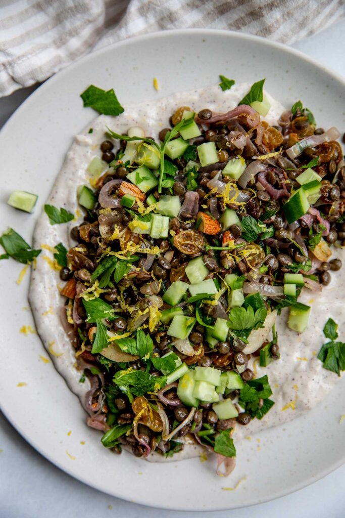 Plate of yogurt topped with lentil salad, cucumber and fresh herbs.