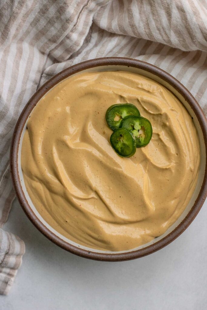 Bowl of cashew cheese sauce topped with 3 slices of jalapenos.