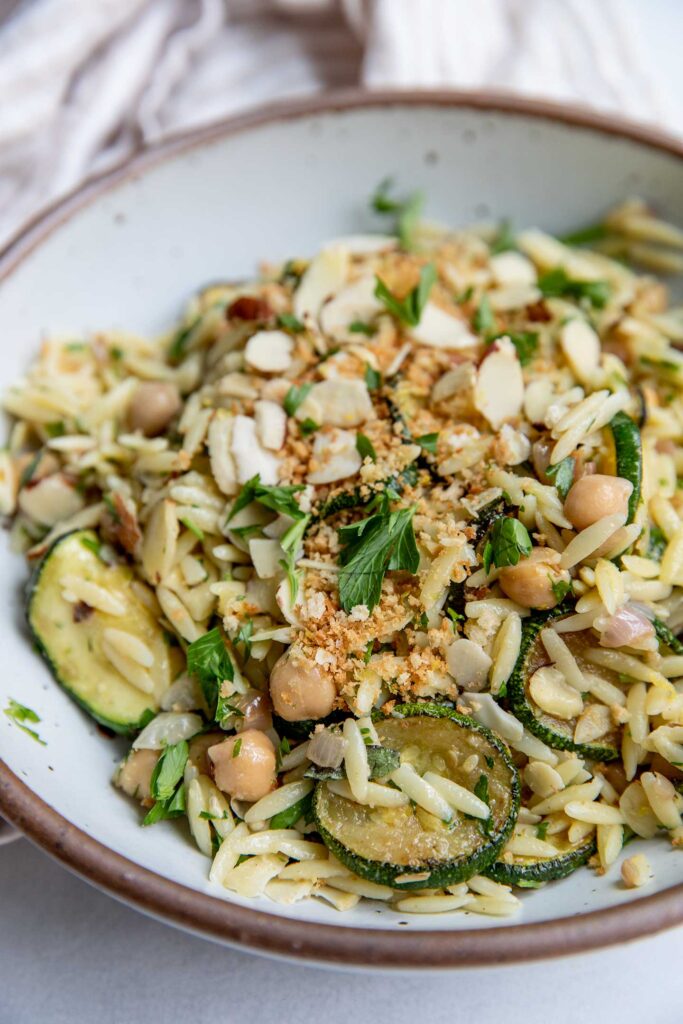 Side view of a bowl of zucchini orzo topped with toasted bread crumbs and almond slices.