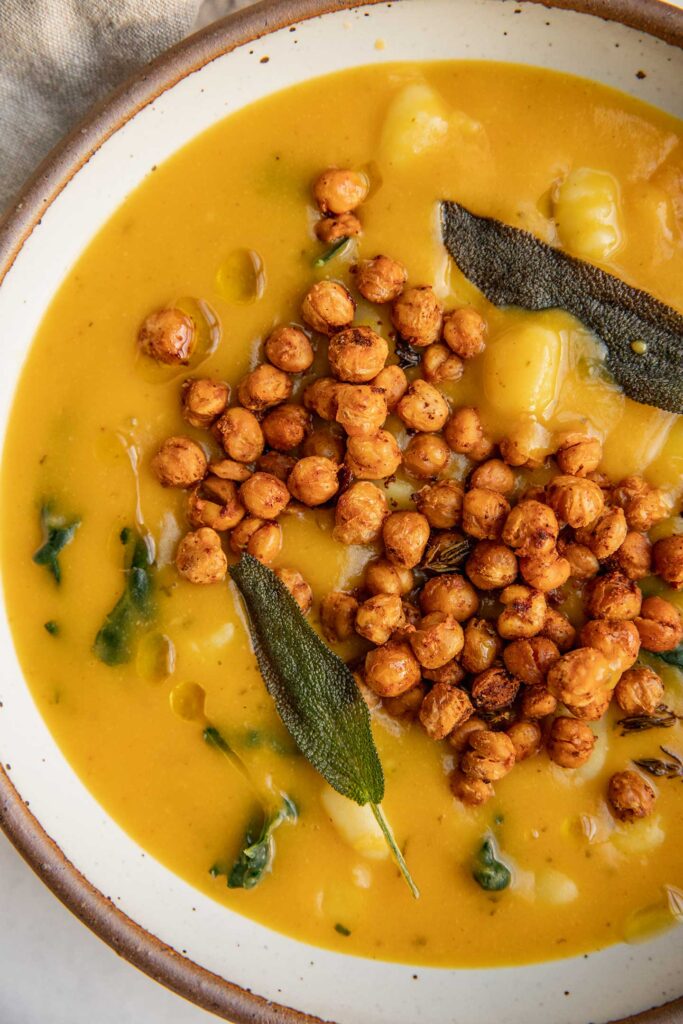 Close up of a bowl of butternut squash soup with kale and gnocchi topped with crispy chickpeas and sage.