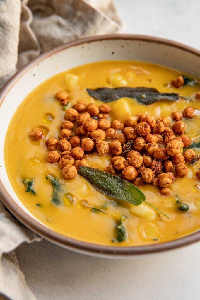 Side view of a bowl of butternut squash gnocchi soup topped with roasted chickpeas and crispy sage leaves.