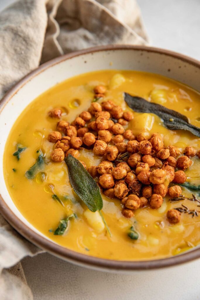 Close up side view of a butternut squash and gnocchi soup topped with crispy chickpeas and sage leaves.