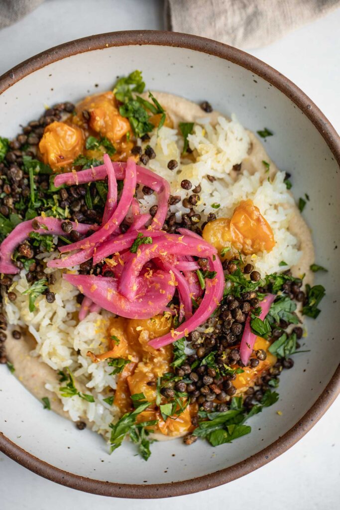 Hummus bowl topped with crispy rice, lentils, stewed tomatoes, and pickled red onions.