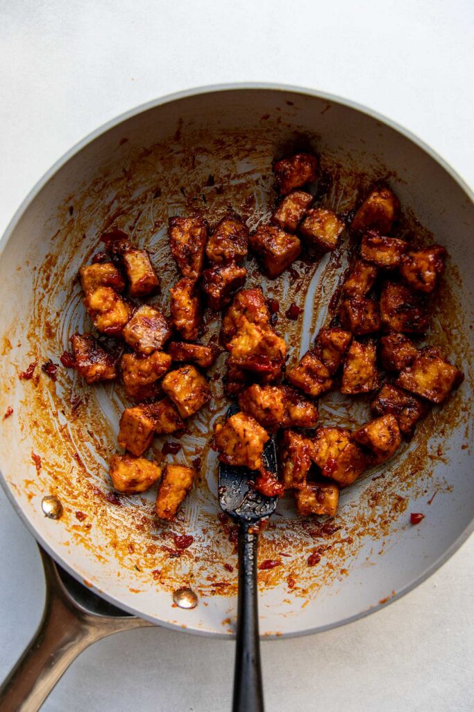 Harissa glazed tofu in a sauce pan with a spatula.