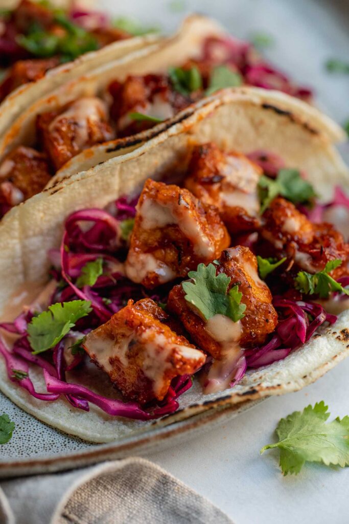 Close up of an open tortilla filled with red cabbage slaw and harissa glazed tofu.