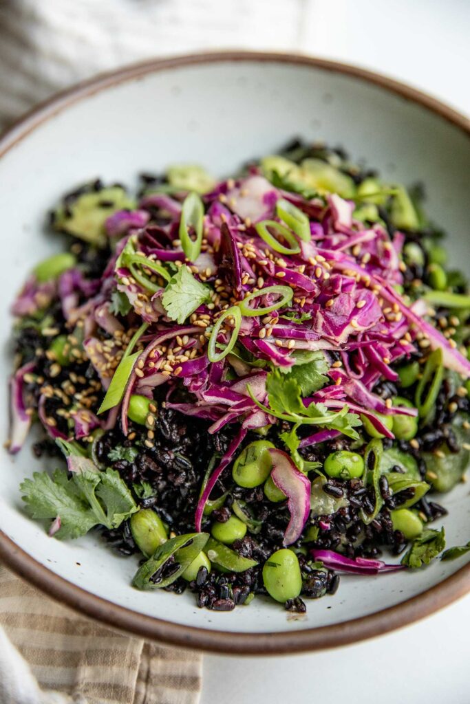 Side view of black rice salad topped with red cabbage slaw and extra scallions.