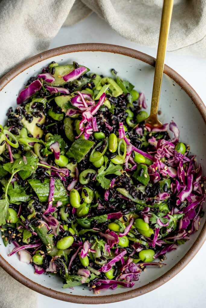Mixing of black rice salad with red cabbage slaw with a spoon in a bowl.