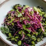 Side view of a salad made with black rice, edamame, and avocado topped with cabbage slaw.