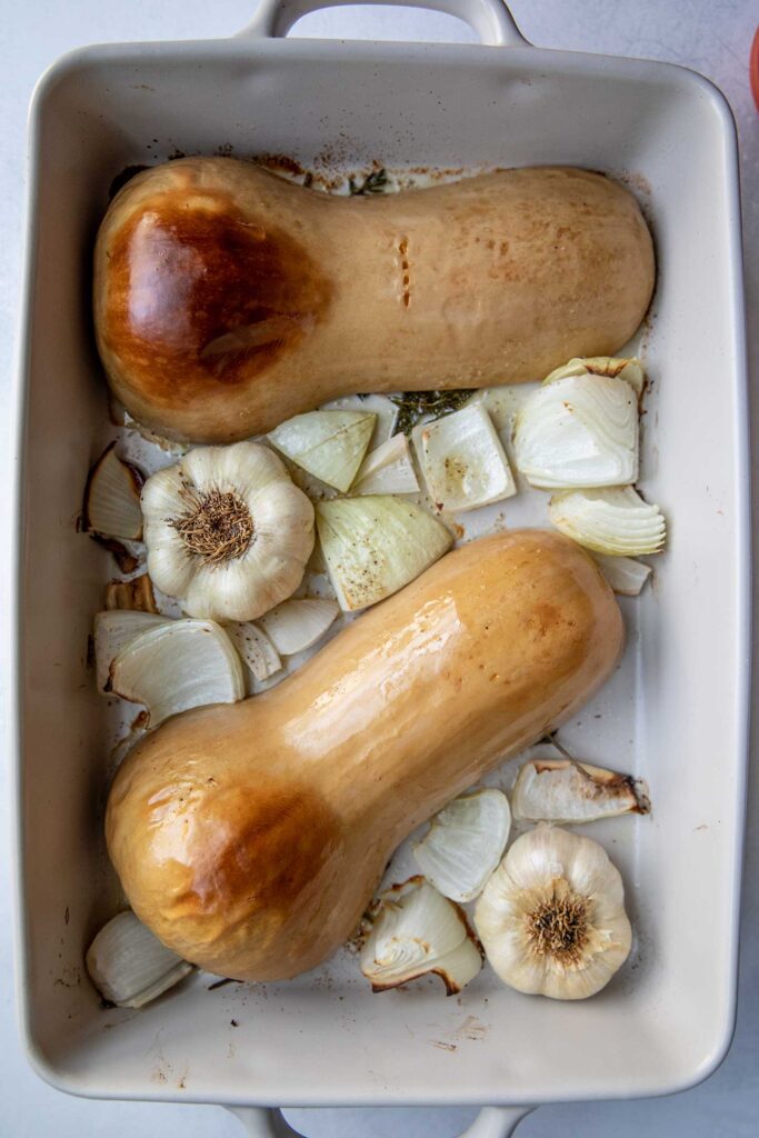 Roasted butternut squash, garlic bulbs and onion in a baking dish.