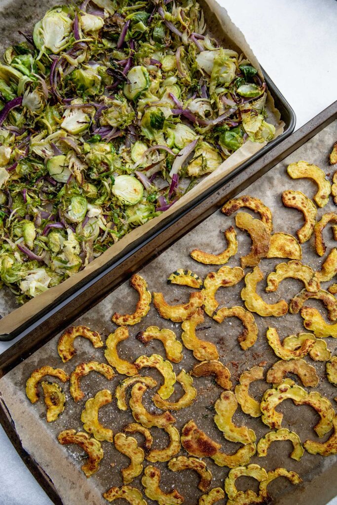 One tray with roasted delicata squash and a seperate sheet pan of roasted brussels sprouts.