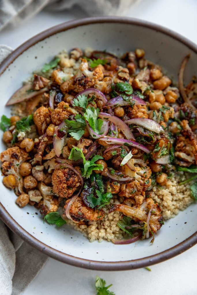 Close up of a bowl of quinoa topped with maple lime roasted cauliflower and crispy chickpeas and walnuts.
