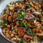 A side view of a bowl of quinoa topped with roasted cauliflower, marinated onions and crispy chickpeas.