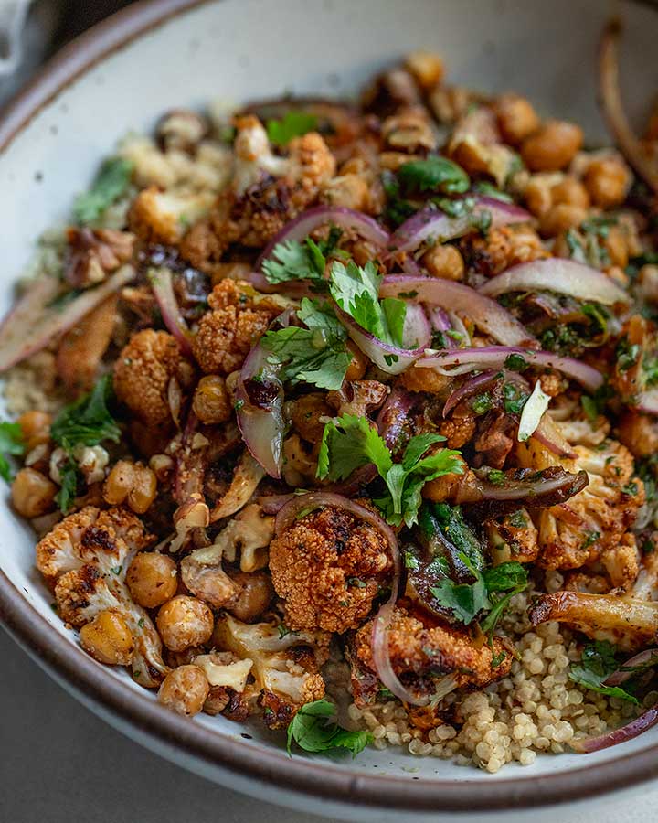 A side view of a bowl of quinoa topped with roasted cauliflower, marinated onions and crispy chickpeas.