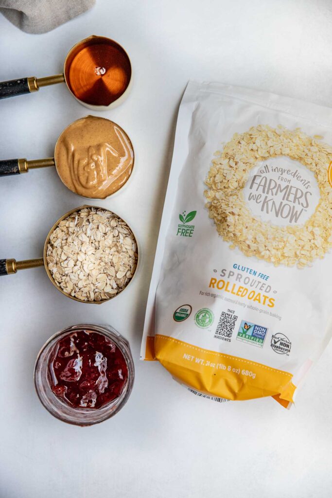 Bag of One Degree Organics Rolled Oats next to a line of measuring cups filled with maple syrup, peanut butter, oats and jelly.