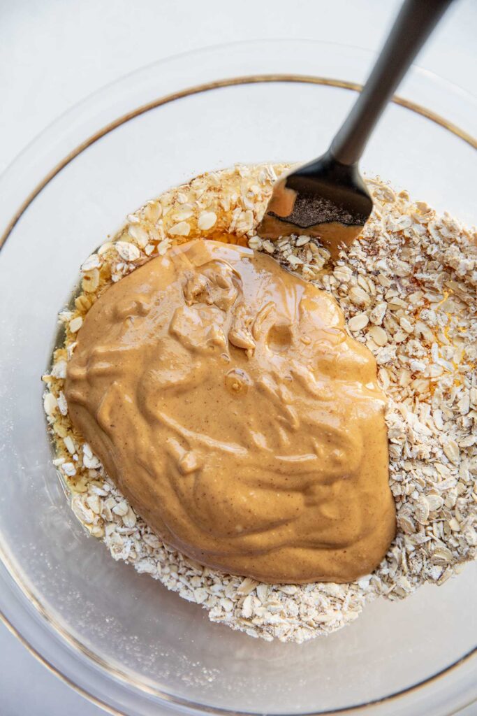 Mixing the oatmeal, peanut butter, and maple syrup together in a glass bowl.
