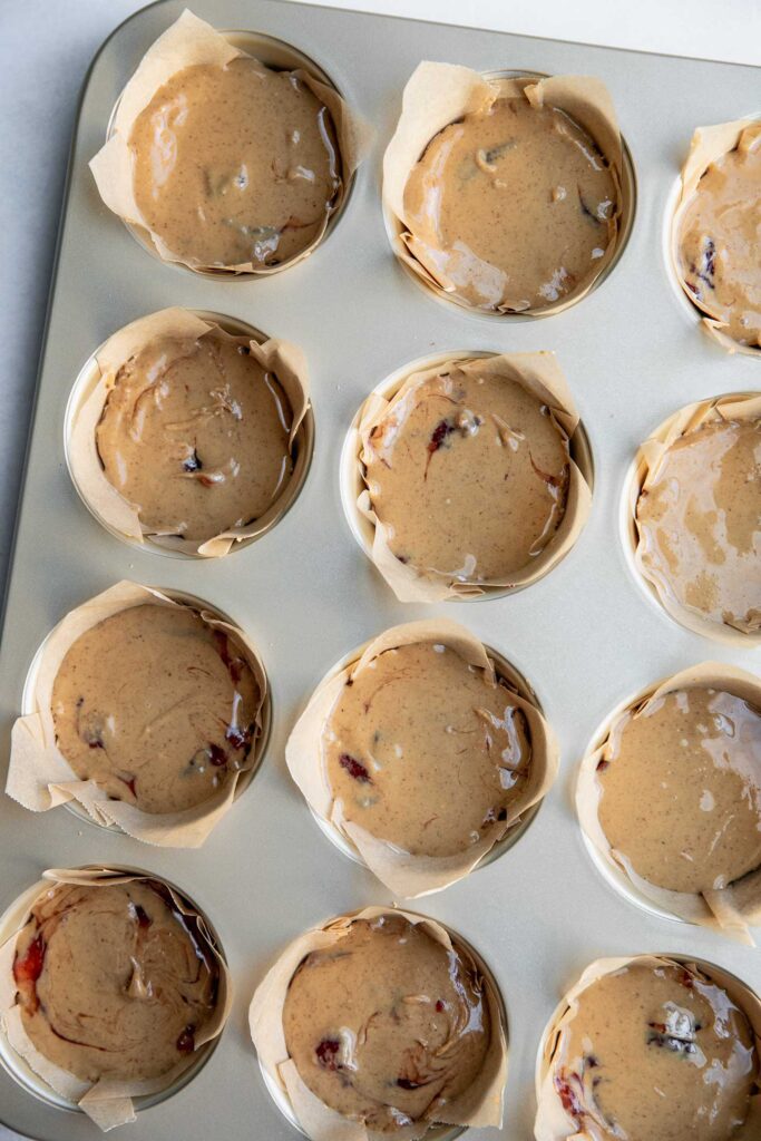 Smoothing out the peanut butter layer of the oat cups in a muffin tin.