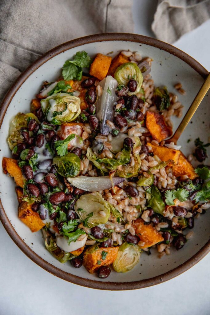 Mixing together the farro, roasted butternut squash, brussels sprouts, black beans and yogurt sauce together with a gold spoon.