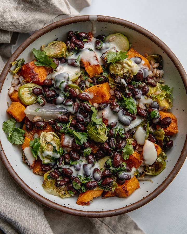 Bowl of marinated black beans on top of a mix of farro, crispy butternut squash, and brussels sprouts.