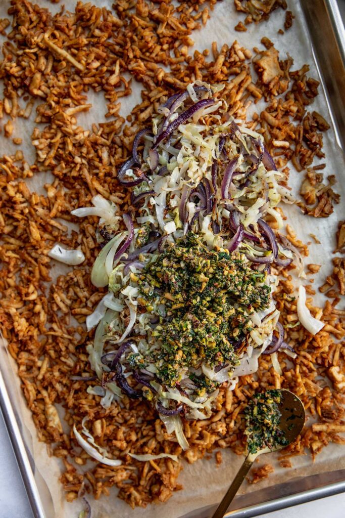 A baking tray filled with shredded baked tofu, cabbage, onions and herby pistachio za'atar.