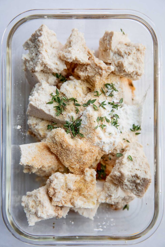 Tofu chunks in a container with corn starch, corn meal, seasonings and soy sauce.