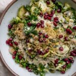 Toasted quinoa salad topped with pomegranate seeds in a white bowl.