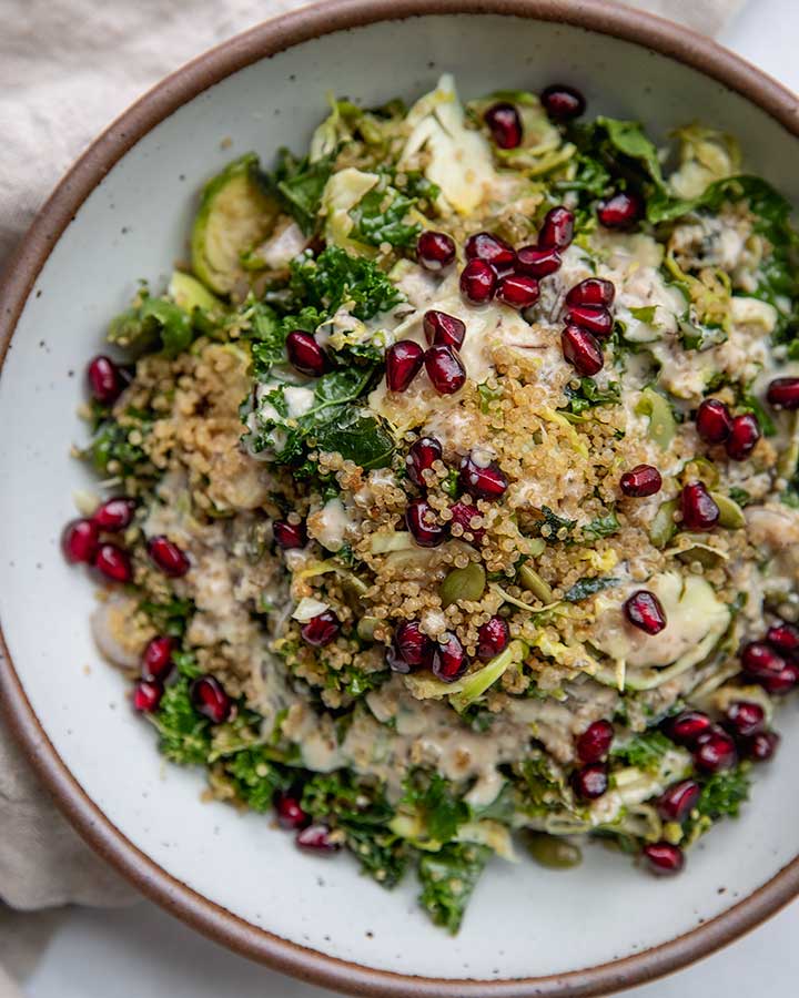 Toasted quinoa salad topped with pomegranate seeds in a white bowl.