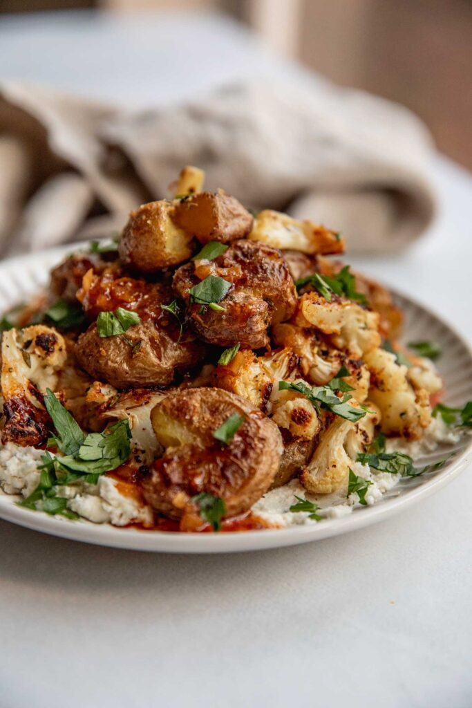 Plate of spreadable dairy-free cheese topped with roasted cauliflower, potatoes and hot maple sauce.