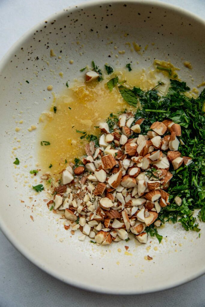 Lemon juice, maple syrup, almonds, herbs and mustard in a bowl to be mixed.