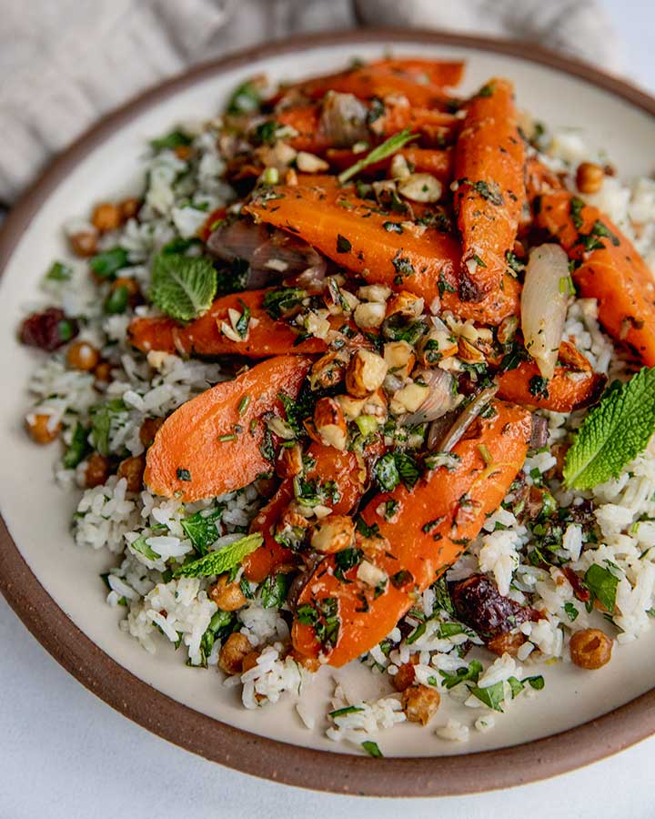 Serving platter filled with rice salad and topped with glazed carrots, almonds and herbs.